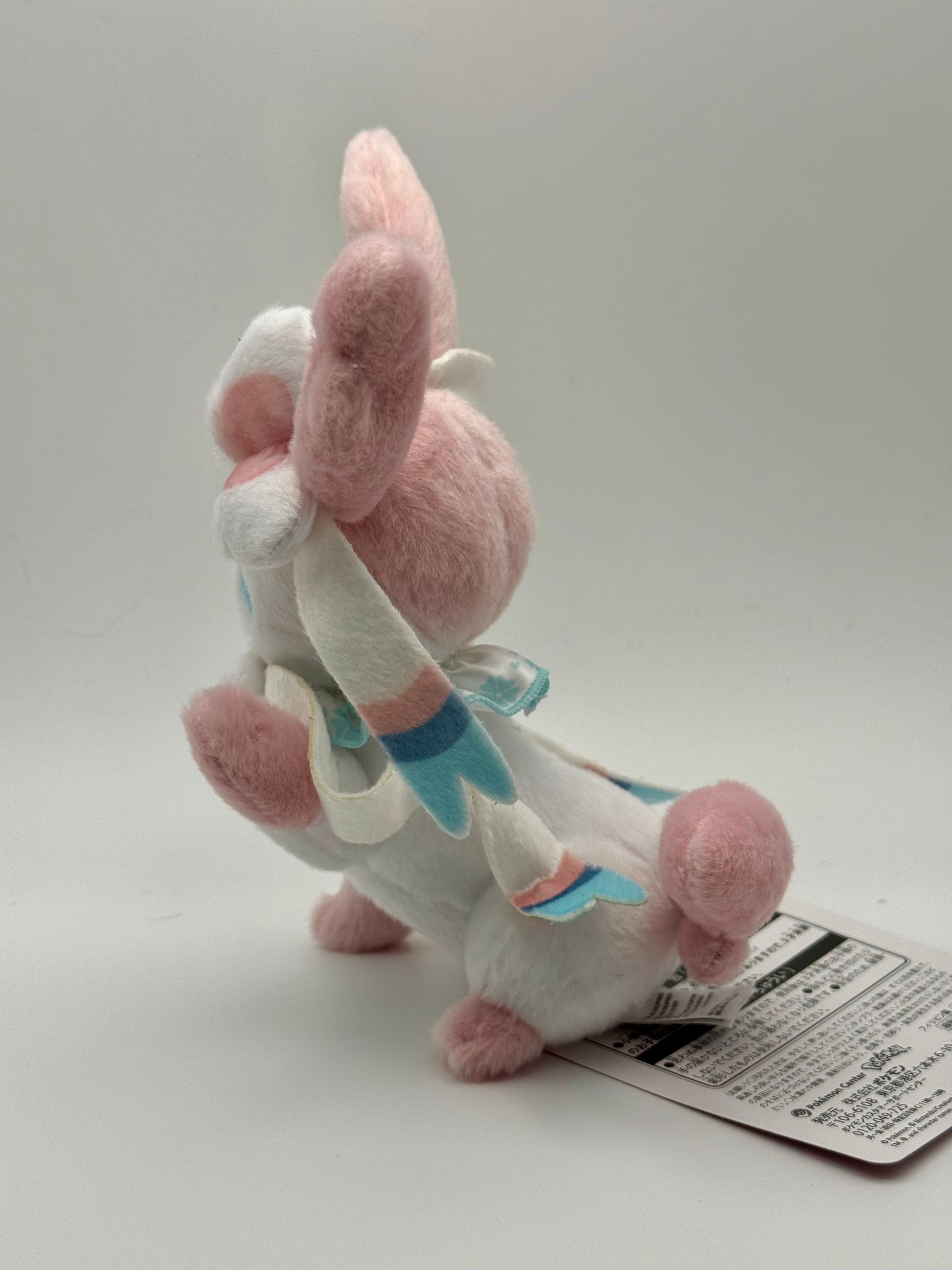 Eevolvd Sylveon Plush med vinkandes och sittandes pose sedd fran vanster sidan direkt fran Pokemon Center Japan