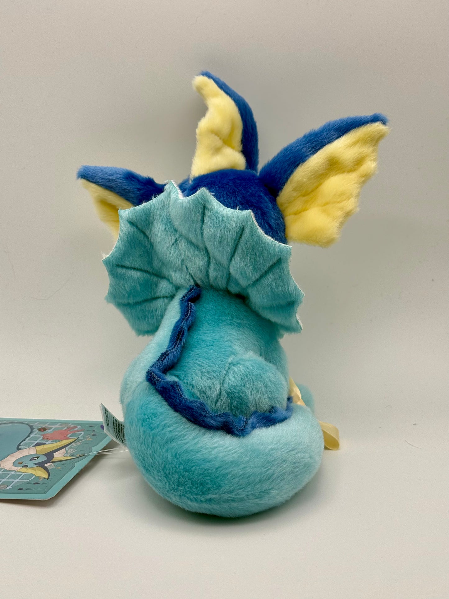 Eevolvd Vaporeon Plush med vinkande tass och sittandes med ett leende sedd bakifran direkt fran Pokemon Center Japan