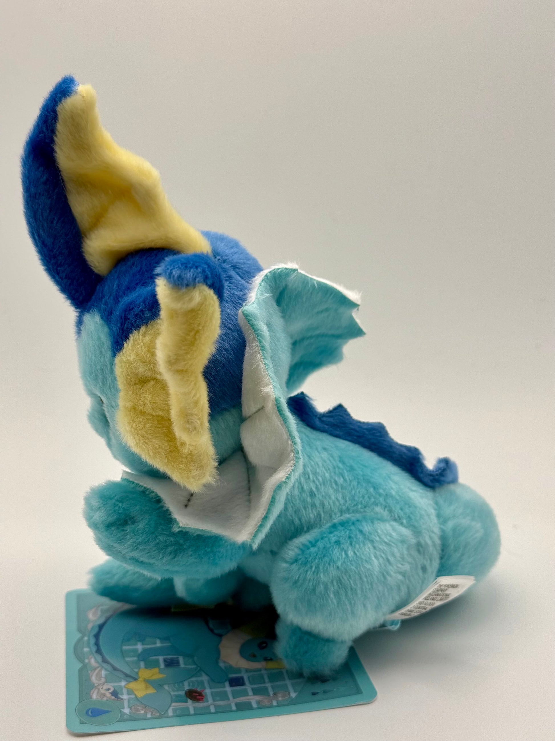 Eevolvd Vaporeon Plush med vinkande tass och sittandes med ett leende sedd fran vanster sida direkt fran Pokemon Center Japan